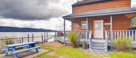 Une cabane en bois avec une véranda, une pancarte indiquant « ici, c’est la plage », et une table de pique-nique.