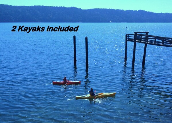 Two kayaks on a calm lake with a dock and a forested hill in the background.
