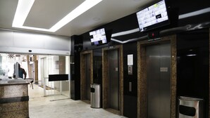 A modern elevator area with granite walls, a digital display, and a trash bin. - Rio Rentals 021- C047 Studio na quadra da praia com máquina (Rio de Janeiro)