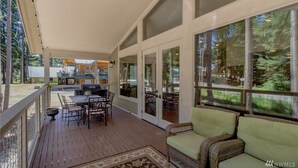A covered deck with outdoor furniture, large windows, and a view of the surrounding forest. - Lake Cabins Lodge (Cle Elum)