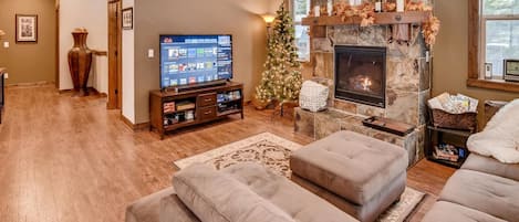 A cozy living room with a stone fireplace, a flat-screen TV, and a Christmas tree.