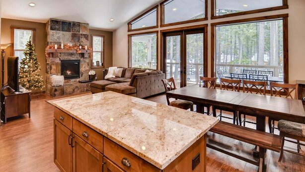 A spacious kitchen with a large island, a fireplace, and a dining area with a view of the forest. - Lake Cabins Lodge (Cle Elum)