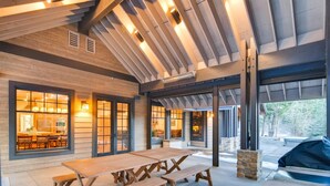 A spacious indoor area with a large wooden table and benches, large windows with warm lighting, and a view of the outside. - Pine Ridge Estate (Cle Elum)