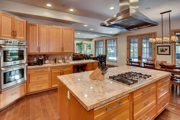A modern kitchen with wooden cabinets, stainless steel appliances, a marble countertop, and a large island with a gas stove.