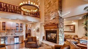 A spacious living area with a stone fireplace, a kitchen with wooden cabinets, and a dining area. - Pine Ridge Estate (Cle Elum)