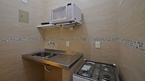 A compact kitchenette with a microwave, sink, and gas stove. - Rio Rentals 021- C074 Studio na quadra da praia de Copacabana (Rio de Janeiro)