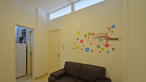 A living room with a brown sofa, a white coffee table, and a wall with colorful floral decals. - Rio Rentals 021- C074 Studio na quadra da praia de Copacabana (Rio de Janeiro)