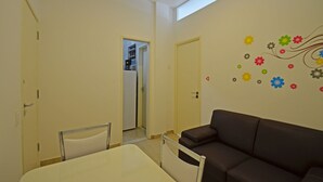 A room with a brown leather sofa, a white table, and a door leading to a kitchen. - Rio Rentals 021- C074 Studio na quadra da praia de Copacabana (Rio de Janeiro)