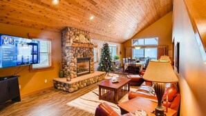 Una sala de estar acogedora con chimenea de piedra, un árbol de Navidad, muebles de cuero y un televisor que muestra un menú.