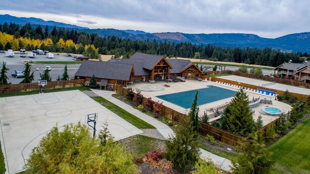Una cabaña con piscina, cancha de baloncesto y montañas al fondo.
