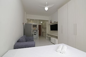 A modern hotel room with a bed, a grey sofa, a TV, and a wardrobe.