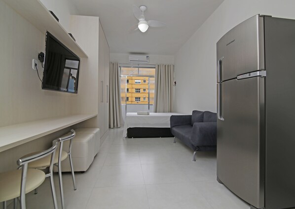 A modern hotel room with a kitchenette, a sofa, a dining area with a bar stool, and a large refrigerator.