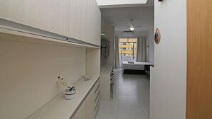 Um corredor estreito com uma área de cozinha à direita, destacando bancada, pia e armários. Um ventilador de teto é visível ao fundo.