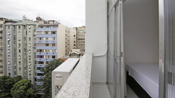 Varanda com vista para edifícios próximos, uma cama e uma janela.