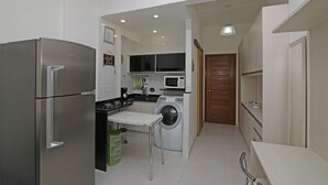 Uma cozinha compacta com geladeira de aço inoxidável, máquina de lavar, micro-ondas e pia.