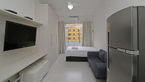 Quarto de hotel moderno com televisão de tela plana, uma cama, um sofá, um refrigerador e um ventilador de teto.