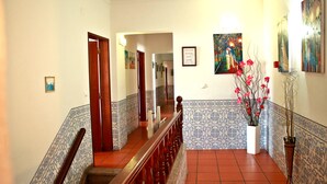 Un pasillo con escalera de madera, paredes de baldosas y una planta en maceta con flores rosadas.