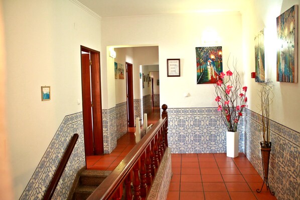 A hallway with a wooden staircase, tiled walls, and a potted plant with pink flowers. - Hotel Santa Comba (Moura)