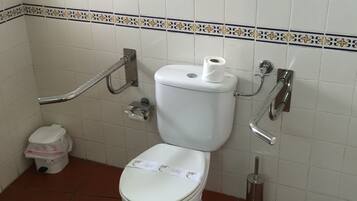 Une salle de bain standard avec des toilettes blanches, un bidet, une poubelle et un porte-rouleau de papier toilette.