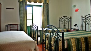 Habitación con dos camas, un escritorio y una silla. Se aprecia una ventana con cortinas, una lámpara sobre el escritorio y un cartel rojo en la pared.