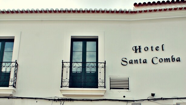 Un edificio con un letrero que dice "Hotel Santa Comba" y un toldo amarillo. Hay plantas en macetas frente a la entrada.