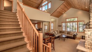 A spacious living area with a wooden staircase, a stone fireplace, and large windows. - Roslyn Hideaway (Cle Elum)