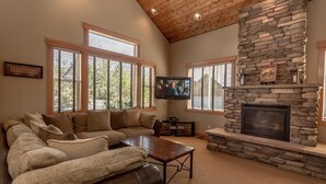 A living room with a stone fireplace, a leather sofa, and a television mounted on the wall. - Roslyn Hideaway (Cle Elum)