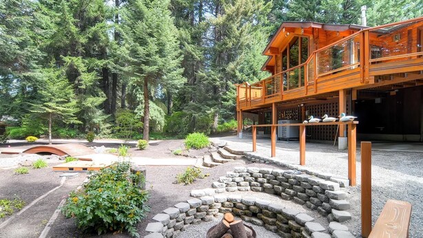 A wooden cabin with a deck and a stone fire pit surrounded by a garden. - Yakima River Retreat (Cle Elum)