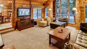 A cozy log cabin interior with a television, leather sofas, and a dining area. - Yakima River Retreat (Cle Elum)