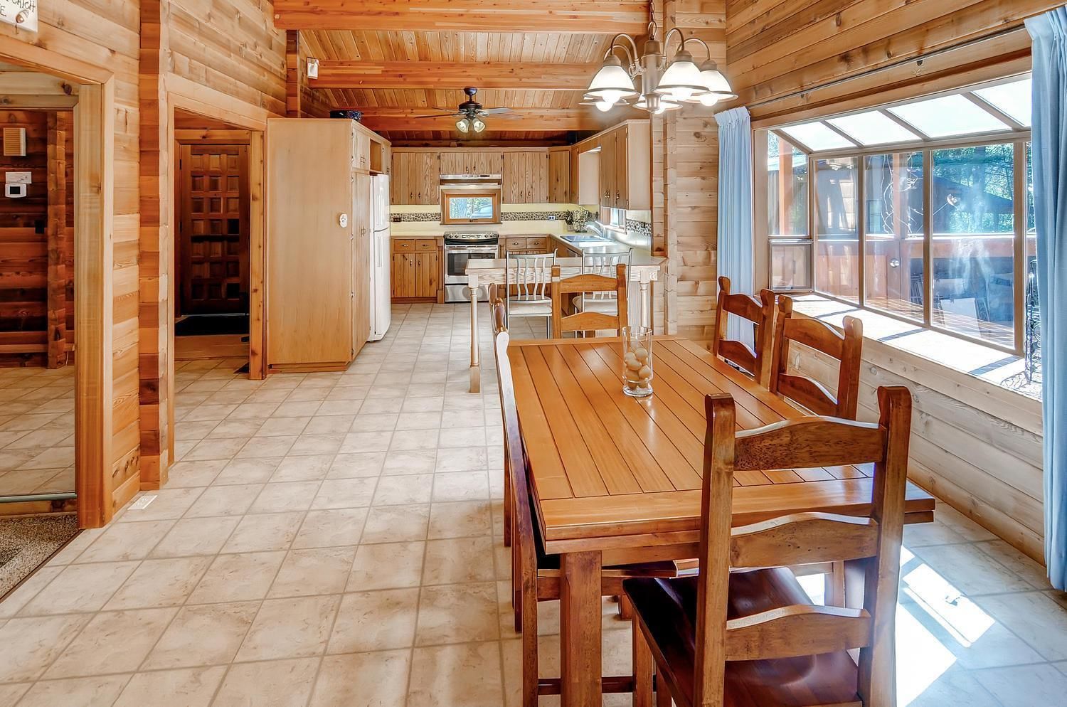 L’intérieur d’un chalet en bois comprend une table à manger, des chaises, un coin cuisine et de grandes fenêtres.