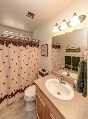 Une salle de bain équipée de toilettes, d’un lavabo et d’un rideau de douche orné de motifs représentant des arbres à feuilles de pin.