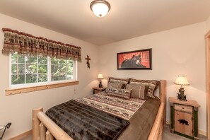 Une chambre avec un grand lit, une fenêtre donnant sur des arbres, un crucifix au mur et un tableau sur le thème des ours.