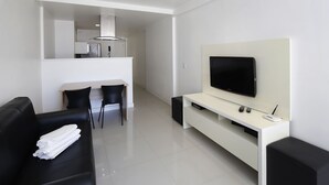 Ein modernes Wohnzimmer mit einem schwarzen Sofa, einem flachbildfernseher an einer weißen Unterhaltungsecke und einer Küchenzeile im Hintergrund.