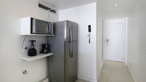 Eine kompakte Küche mit einem Edelstahlkühlschrank, einer Mikrowelle und einer Kaffeemaschine auf einem weißen Regal.