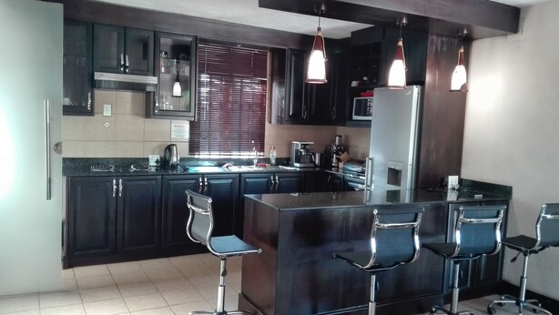 Une cuisine moderne avec des meubles de couleur sombre, un îlot central en acier inoxydable et des tabourets de bar.