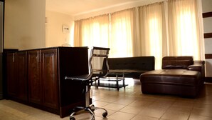 Un salon comprenant un meuble en bois foncé, un fauteuil de bureau noir, un canapé en cuir marron et un pouf en cuir marron.