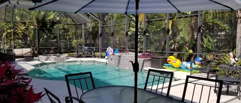 A pool area with a covered seating area, a hot tub, and a waterfall feature.