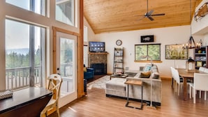 A spacious living room with a high ceiling, large windows, a fireplace, and a dining area. - Roslyn Ridge Retreat (Cle Elum)
