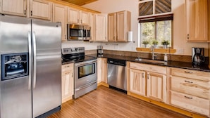 A modern kitchen with stainless steel appliances, wooden cabinets, and a brick backsplash. - Roslyn Ridge Retreat (Cle Elum)
