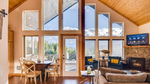 A spacious living area with a large fireplace, multiple windows offering views of the outdoors, and a television mounted on the wall. - Roslyn Ridge Retreat (Cle Elum)