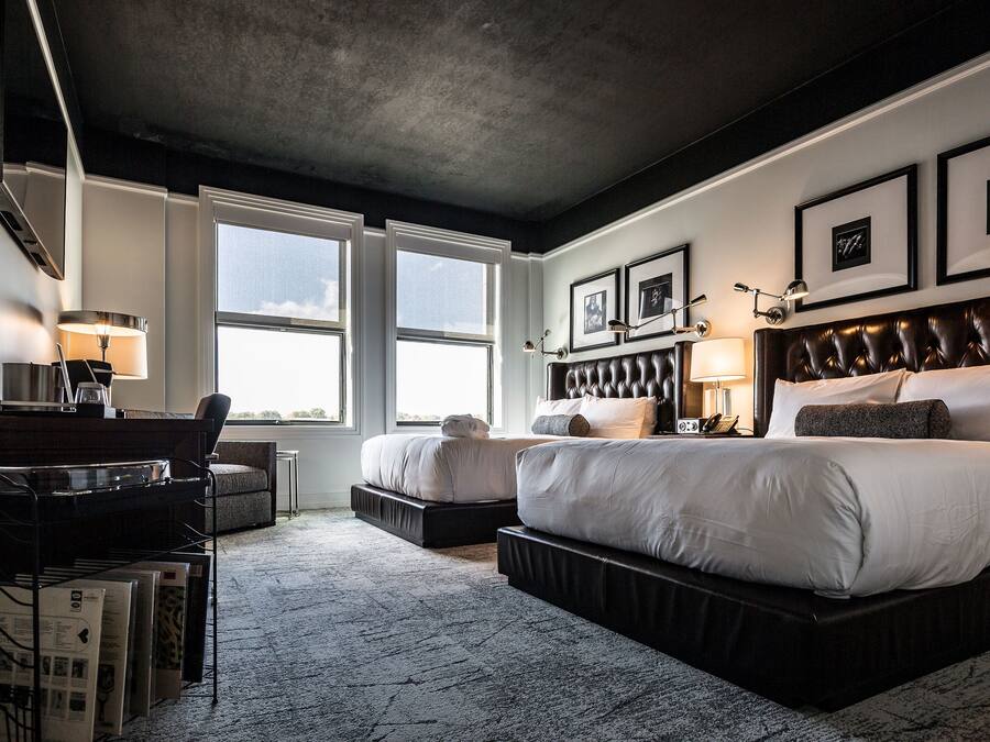 Une chambre d’hôtel moderne, dotée d’un grand lit, d’un bureau et d’une chaise. Deux fenêtres laissent entrer la lumière naturelle.