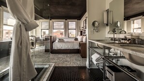 A modern hotel room with a large bed, a bathroom with a large mirror and sink, and a view of buildings outside.