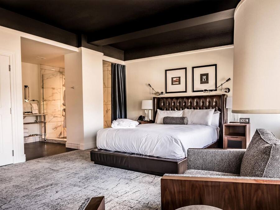 A modern hotel room with a large bed, a sitting area with a sofa, a bedside table, and a nightstand.