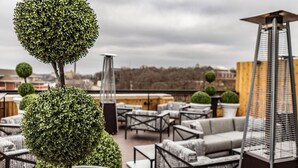A rooftop terrace with round potted plants, outdoor furniture, and a modern lamp.