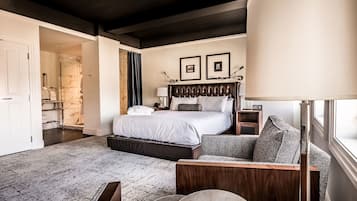 A hotel room with a large bed, a sitting area with a sofa and armchair, a small bedside table, a nightstand, a lamp, and a framed picture on the wall.