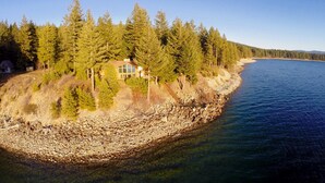 Une maison située sur la côte, entourée d’une forêt dense, avec un rivage rocheux et une vue dégagée sur l’océan.