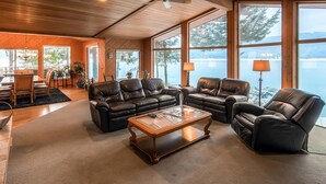 Un salon spacieux, doté de canapés en cuir, d’une table basse en bois et de grandes fenêtres offrant une vue sur un lac.