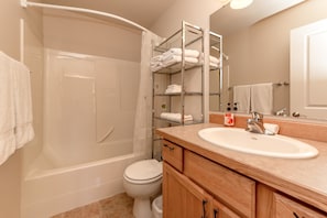 Une salle de bain équipée d’une baignoire, de toilettes, d’un meuble-lavabo avec un évier et d’un porte-serviettes où sont soigneusement pliées les serviettes.