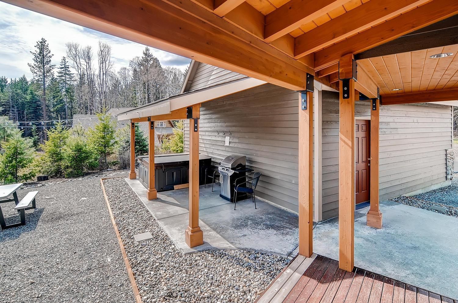 A covered outdoor area with a barbecue grill, seating, and a wooden deck.
