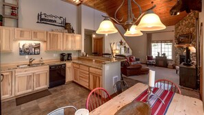 A spacious kitchen with wooden cabinets, a central island, and a dining area with a red chair and a table. - Wintergreen Chalet (Cle Elum)